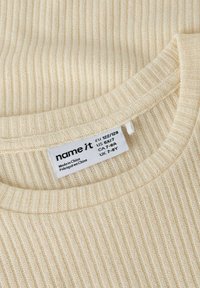 Beżowy prążkowany sweter z zaokrąglonym dekoltem i fakturowaną tkaniną. Dołączona metka pielęgnacyjna z informacjami o rozmiarze i szczegółami produkcji.