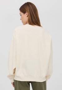 Felpa color crema, oversize, con polsini e orlo a costine. Tessuto morbido, vestibilità rilassata e scollatura arrotondata, con spalle cadenti.