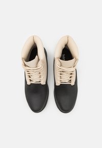 Botas impermeables en negro y beige con una superficie texturizada, punta redondeada y cordones en contraste, que cuentan con un cuello acolchado para mayor comodidad.