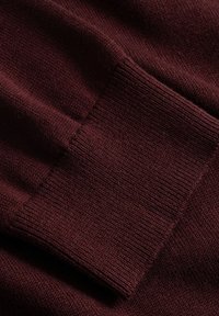 Κοντινή λήψη ενός διπλωμένου πλεκτού υφάσματος σε σκούρο βουργουνδί χρώμα που δείχνει λεπτομερή υφή με ριμπ μανσέτα.