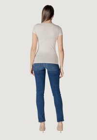 Top beige de manga corta combinado con unos jeans ajustados azules, destacando un acabado de tejido suave y un diseño de pierna ajustada. Fondo claro y neutro.