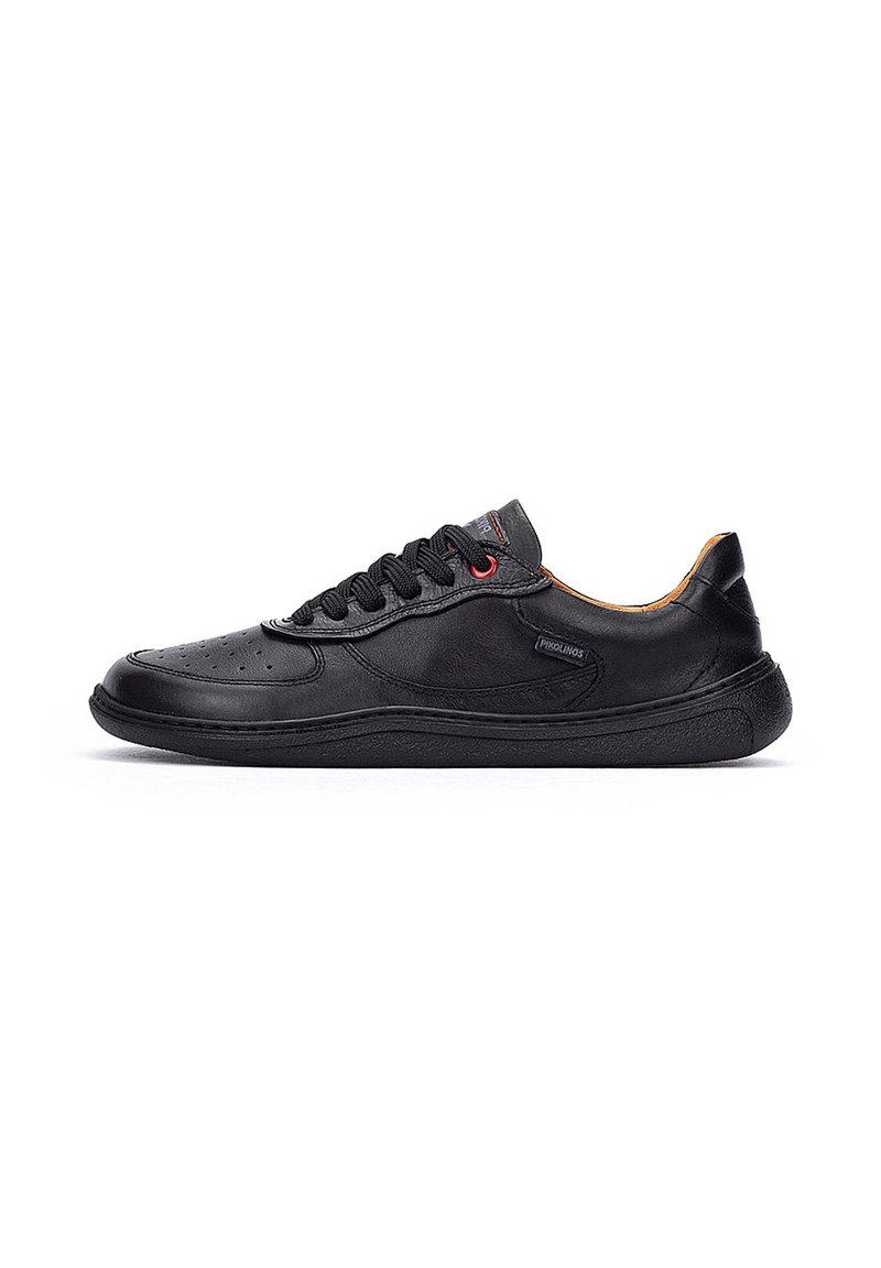 Zapatilla de cuero negro con superficie texturizada, puntera redonda, suela de goma plana y ojetes para cordones en contraste rojo. Diseño minimalista, silueta de caña baja.