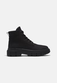 Botte noire montante à lacets avec semelle épaisse et robuste, languette au talon, logo embossé sur le côté et tige en tissu.