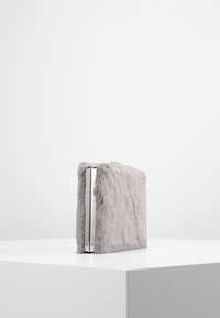 Portefeuille en fausse fourrure grise avec un cadre argenté élégant, présentant une surface texturée et une forme rectangulaire. Design compact et minimaliste.