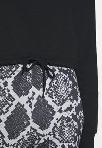 Felpa nera con cordino all'orlo abbinata a leggings a fantasia con un design a serpente in bianco e nero.
