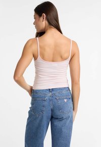 Débardeur rayé rose clair avec des bretelles fines, associé à un jean en denim bleu taille haute avec deux poches arrière et une petite étiquette de logo.