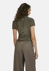 Glinsterend donkergroen kortom met een aangesloten taille, gecombineerd met lichtbruine broek met wijde pijpen en achterzakken.