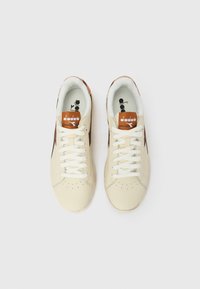 Ζευγάρι από κρεμ και καφέ αθλητικά παπούτσια Diadora με λευκά κορδόνια, βλέποντας από πάνω σε απλό λευκό φόντο.