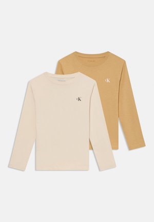 Deux t-shirts à manches longues et col rond, un beige et un moutarde, chacun avec un petit logo "cK" sur la poitrine gauche.
