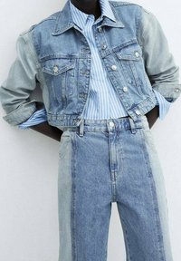 Veste en denim bleu clair avec des boutons en argent, associée à une chemise rayée bleue et blanche, et un pantalon en denim taille haute dans des teintes variées.