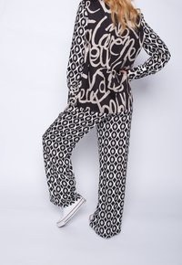 Black and cream two-piece outfit featuring a patterned long-sleeve top with script and loose-fitting pants with an oval design. Ginnastica shoes complete the look.