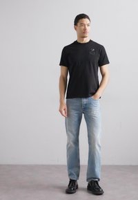 Zwart t-shirt met korte mouwen met een klein logo op de borst, gecombineerd met lichtblauwe rechte jeans en zwarte schoenen. Eenvoudig, strak ontwerp.