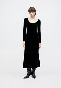 Μαύρο βελούδινο μάξι φόρεμα με μακριά μανίκια και φαρδιά λαιμόκοψη σε σχήμα scoop. Κομψή, απαλή υφή και ραμμένη σιλουέτα, συνδυασμένο με μπότες μέχρι το γόνατο.