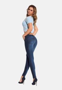 Jeansy typu skinny w ciemnoniebieskim kolorze z wysokim stanem, z dwoma tylnymi kieszeniami i kontrastowym przeszyciem. Połączone z jasnoniebieskim swetrem o kroju cropped.