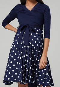 Mörkblå omlottklänning med trekvartslånga ärmar, åtspänd i midjan med ett knytband, har vita prickar på en utsvängd kjol.