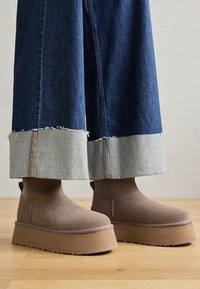 Bottines à plateforme en daim marron avec un bout arrondi et des panneaux latéraux élastiques. Portées avec des culottes en denim bleu à ourlet effiloché.