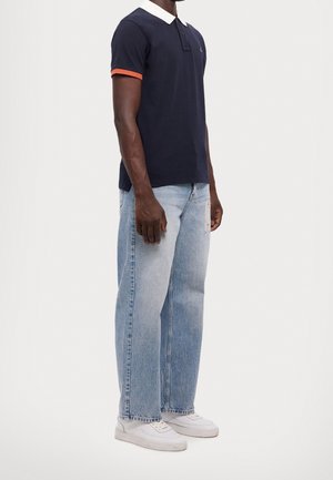 Marineblå polo skjorte med hvid krave og orange detaljer på ærmerne, parret med lyseblå løstsiddende jeans og hvide sneakers.