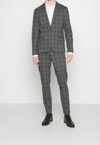 Grårutigt kostym med en enfärgad kavaj, matchande slim-fit byxor och svarta läderskor. Tyget har ett subtilt mönster.
