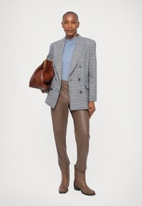 Siva karirana dvoredna blazer jakna, modra majica, rjave usnjene hlače in usnjeni škornji do kolen, ki se ujemajo. Rjav usnjen nahrbtnik z zlatim okovjem.