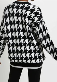 Svart och vit houndstooth-mönstrad tröja i fluffigt material med långa ärmar och ribbad nederdel. Designen är oversize och texturerad.