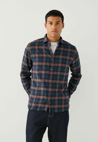 Chemise en flanelle à carreaux avec des couleurs bleu, bourgogne et blanche. Design à boutons, manches longues et coupe décontractée. Texture douce et détail du col.