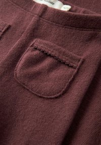 Zbliżenie na miękką, bordową dzianinę z małą kieszonką naszywaną z falbanką.