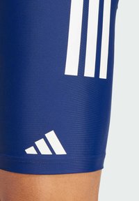 Morske sportske šorceve napravljene od glatkog materijala s bijelim dizajnom s tri pruge. Ima bijeli adidas logo i koso naglašene dijelove na rubu.