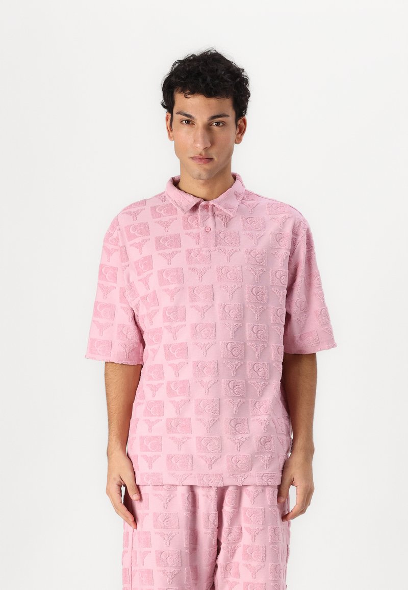 Short-sleeve, pink polo shirt with a textured pattern of squares and stylized motifs, made of soft fabric, featuring a buttoned collar.