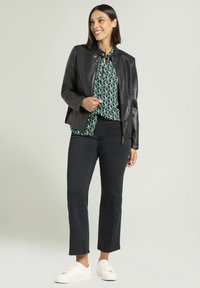 Czarna kurtka z eko skóry z kołnierzem, noszona na zielonej bluzce w wzory. Połączona z ciemnymi dżinsami i białymi tenisówkami. Gładka faktura.