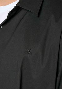 Zwarte kortarmige shirt met een puntige kraag, met een subtiele geborduurde logo op de borst. Gladde stoftextuur.