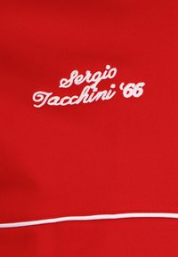 Roter Stoff mit weiß gesticktem Text "Sergio Tacchini '66" und einem weißen horizontalen Streifen im unteren Bereich. Weiche Textur.