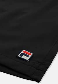 Tissu noir avec un écusson carré cousu affichant une lettre « F » stylisée en bleu marine, blanc et rouge près d'un bord ourlé.