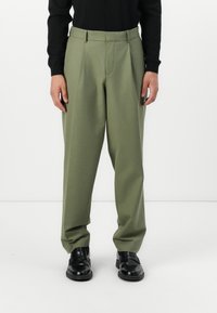 Green tailored trousers with a straight-leg fit, featuring a smooth texture, crease down the front, and subtle pleats at the waistband.