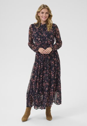Long, navy floral dress with long sheer sleeves, a collar, and a tied waist. Features pink and green floral patterns and a flowing skirt.