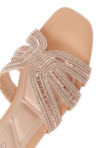 Sandalia deslizante beige con correas trenzadas metálicas y acentos en oro rosa. Plantilla suave con un tacón cuadrado para mayor soporte.