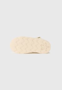Ljusbeige skosula med en vågig textur och stjärnlogotyp, tillverkad av gummi. Har en något rundad tå och platt design.