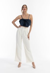 Námorníkově modrý saténový crop top s předním mašlí, zkombinovaný s bílými širokými kalhotami s vysokým pasem. Průhledné podpatky s dekoračními akcenty.