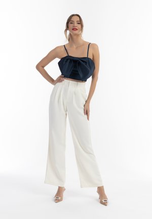 Námorníkově modrý saténový crop top s předním mašlí, zkombinovaný s bílými širokými kalhotami s vysokým pasem. Průhledné podpatky s dekoračními akcenty.