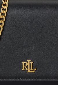 Melna ādas rokassoma ar strukturētu virsmu, ar zelta ķēdes siksnu un izsistā zelta logotipa "RLL" uz priekšējās paneļa.