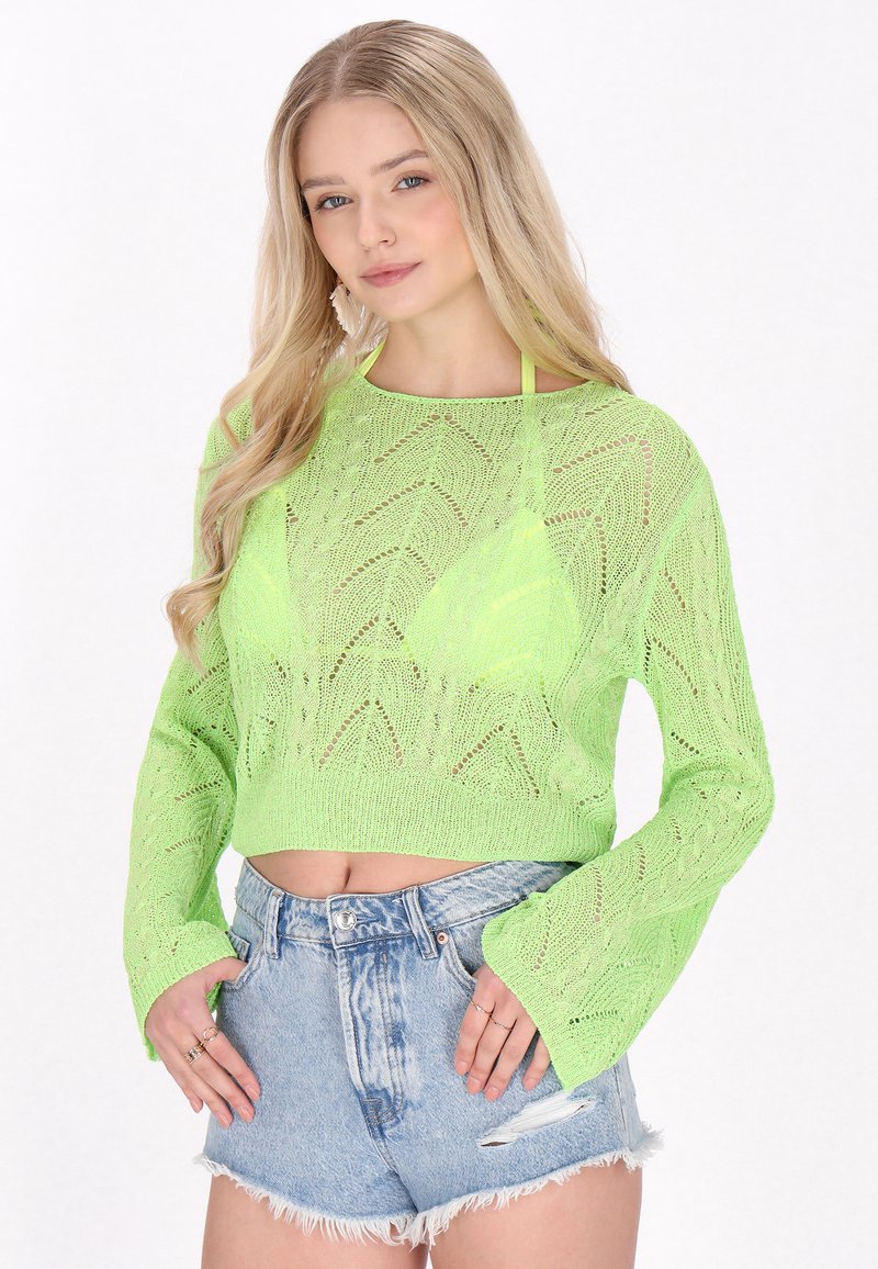 Neon grön stickad kort tröja med ett chevronmönster och trumpetärmar, kombinerad med slitna denimshorts med fransiga kanter.