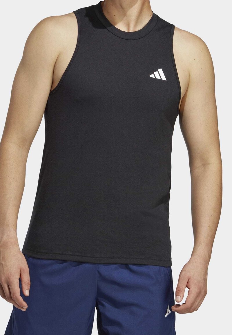 Homme portant un maillot de sport noir sans manches avec un logo blanc et un short de sport bleu avec un logo blanc sur la cuisse gauche, debout devant un fond blanc.