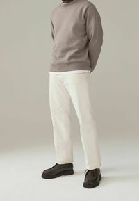 Felpa marrone, camicia bianca sotto, pantaloni crema e scarpe marroni scure. Abbigliamento casual, colori solidi, texture liscia e design minimale.