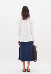 Vit bomullsskjorta med långa ärmar, tillsammans med en knälång denimkjol. Svarta sandaler och en brun tote-väska fulländar outfiten.