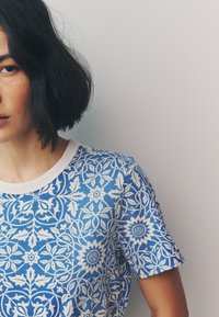 Blau-weißes T-Shirt mit Blumenmuster, Rundhalsausschnitt und kurzen Ärmeln, mit filigranen Designs von Blumen und Blättern.