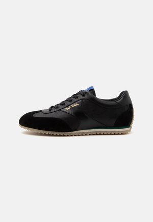 Baskets noires en cuir et suède avec semelle beige rainurée, lacets noirs et logo doré "Paul Smith" sur le côté.
