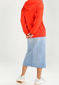 Red hooded jacket, blue denim skirt, white athletic shoes. Smooth fabric with a casual fit; skirt features a frayed hem and side seam detail.