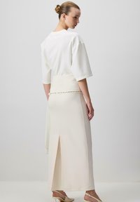 Top bianco a maniche corte abbinato a una gonna maxi fluida color crema con uno spacco laterale e dettagli di bottoni decorativi in vita.
