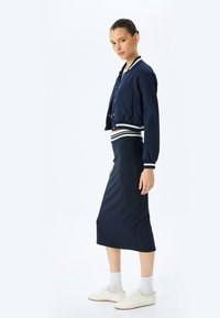 Veste de pilote de la marine avec des poignets rayés, associée à une jupe moulante bleu marine. Tissu doux, design sans coutures et baskets blanches complètent le look.
