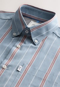 Hellblaues Hemd mit Knöpfen, vertikalen weißen und roten Streifen, mit Kragen, einer Brusttasche und einem eingenähten Markenschild.