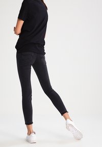 Vaqueros negros ajustados con una textura suave, cintura alta y bolsillos traseros, combinados con una camiseta negra holgada y zapatillas blancas.
